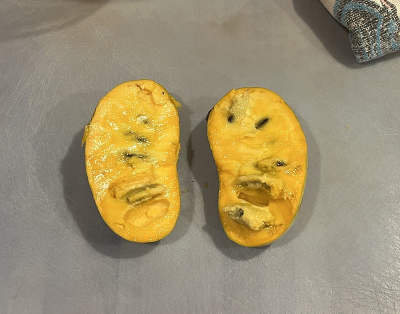 Cut fruit showing creamy orange flesh and large seeds.