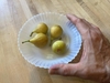 Hand holding a bowl with four, yellow-green fruits.