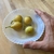Hand holding a bowl with four, yellow-green fruits.
